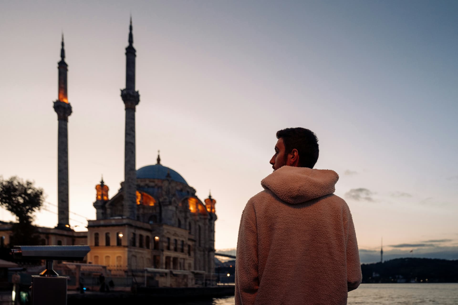 A man gazing at the Ortaköy Mosque on the Bosphorus waterfront at twilight