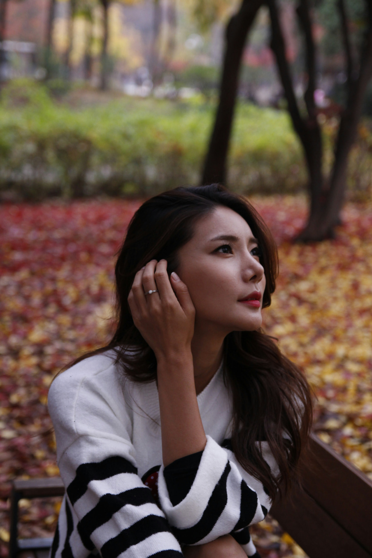 A woman with a thoughtful expression among autumn foliage, resting on a park bench