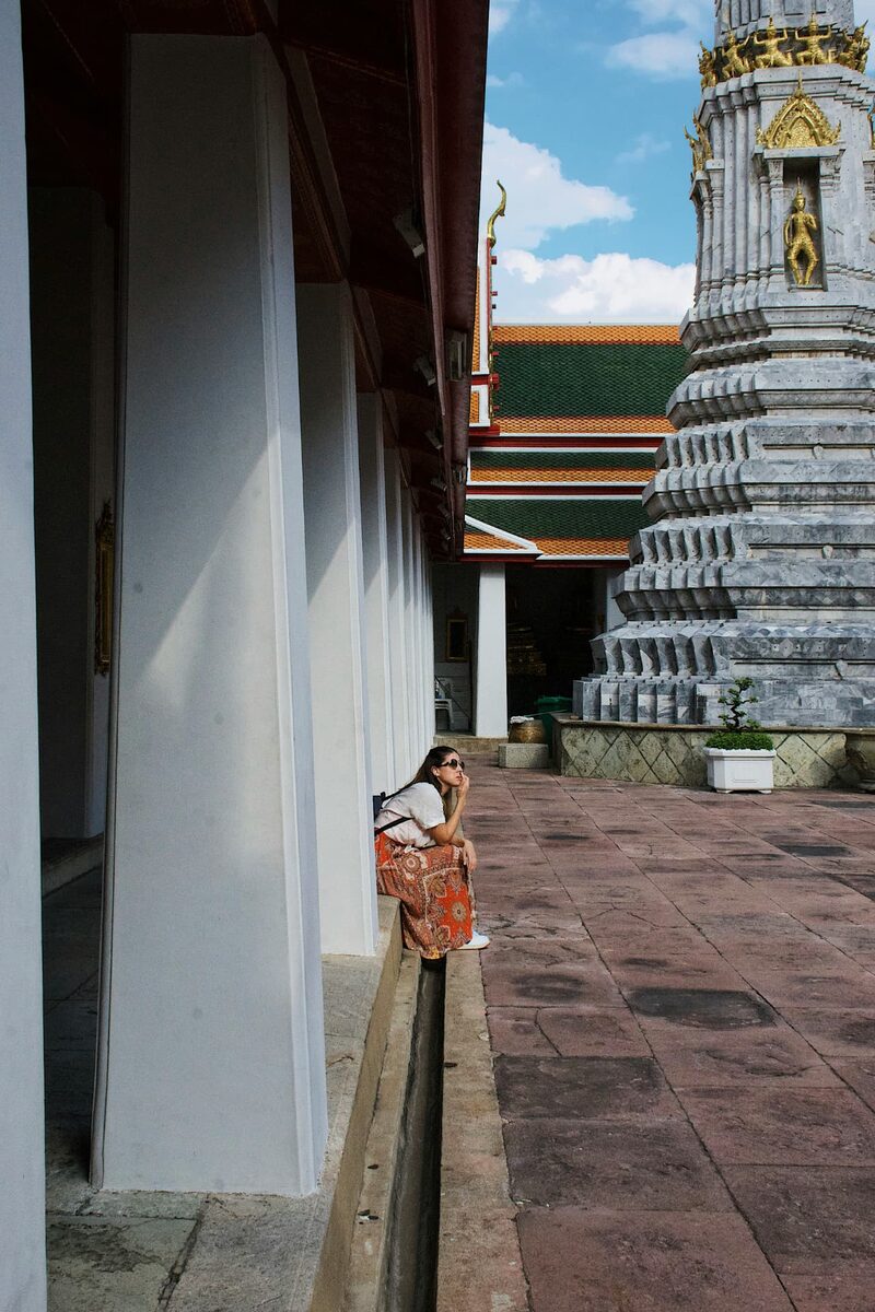 A woman resting at the base of an ornate Bangkok temple prang